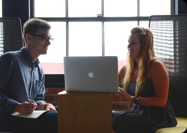 Two people collaborating over a laptop by a window